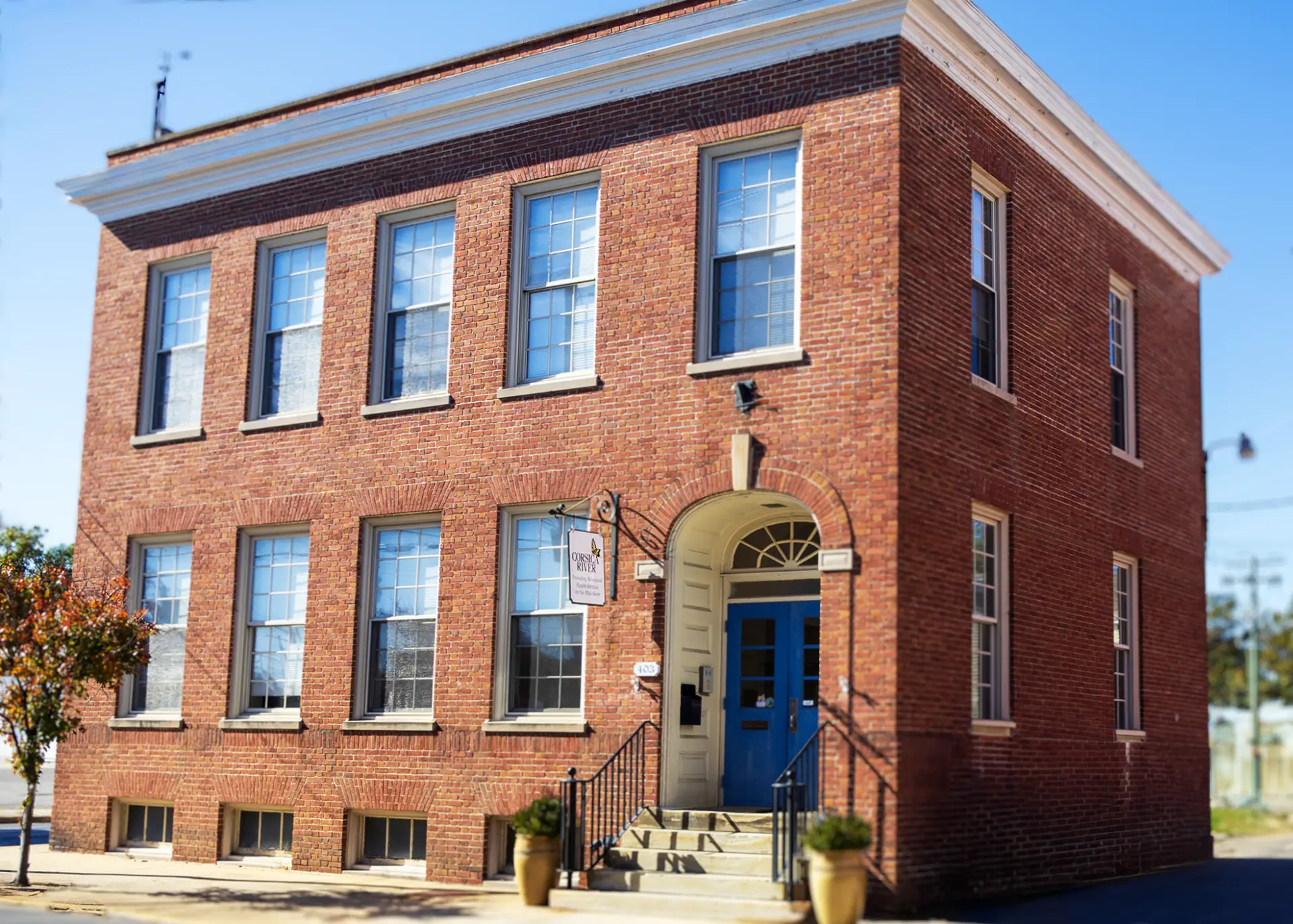 Rivers Crossing Wellness Community office in Cambridge, Maryland located in a historic red-brick building with a blue door.