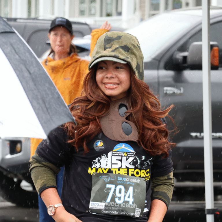Smiling woman in a camouflage hat and Star Wars-themed shirt at a 5K event, wearing race bib number 794 in rainy weather.