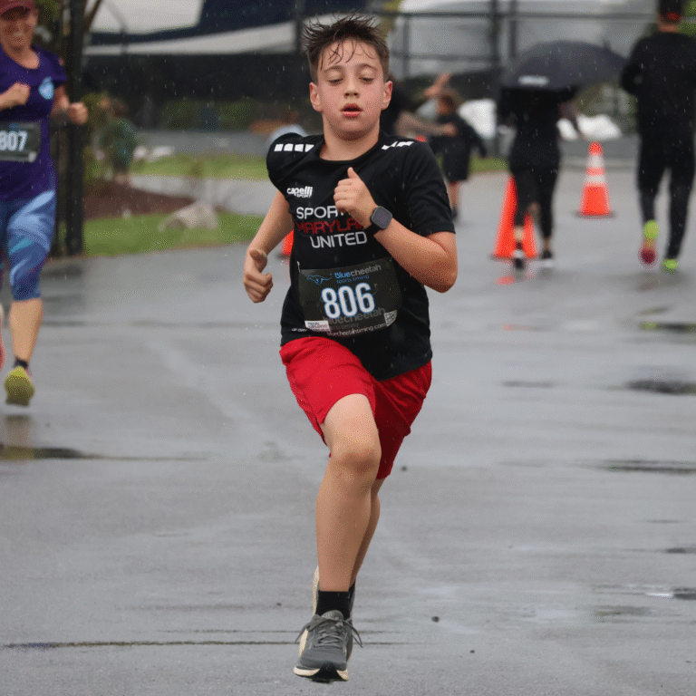 Young boy running in the rain during a 5K race, wearing a black sports shirt and red shorts with race bib number 806.