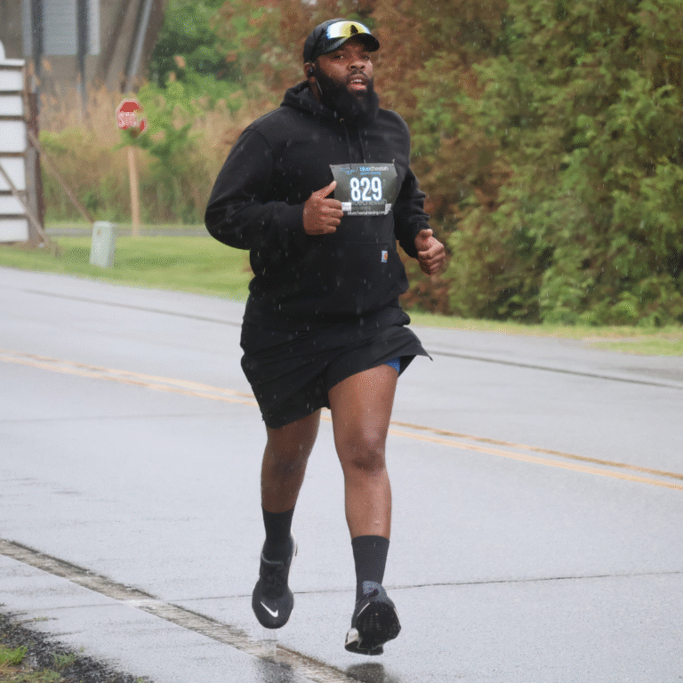 Man running in the rain during a 5K, wearing a black hoodie, shorts, and race bib number 829.