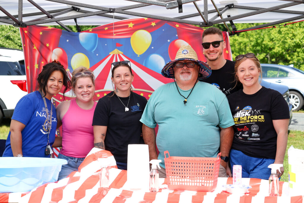 Group of Crossroads Community and Corsica River staff smiling at a carnival-themed booth during community wellness event