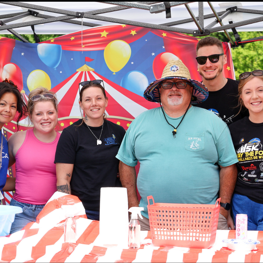 Group of Crossroads Community and Corsica River staff smiling at a carnival-themed booth during community wellness event