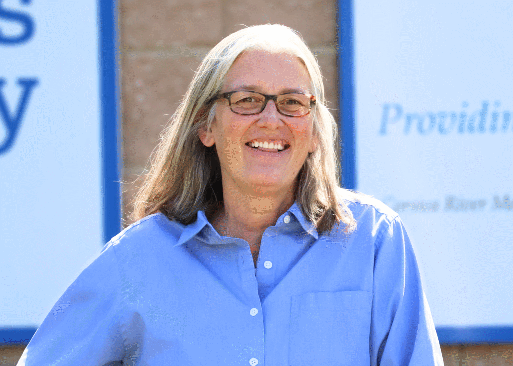 Amy Cheney, Finance Director, smiling in front of Crossroads Community and Corsica River signage.