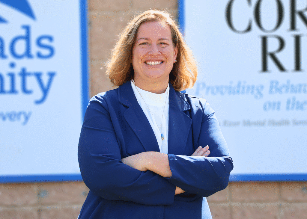 Kara Morris, Acting Executive Director, smiling in front of Crossroads Community and Corsica River signage.