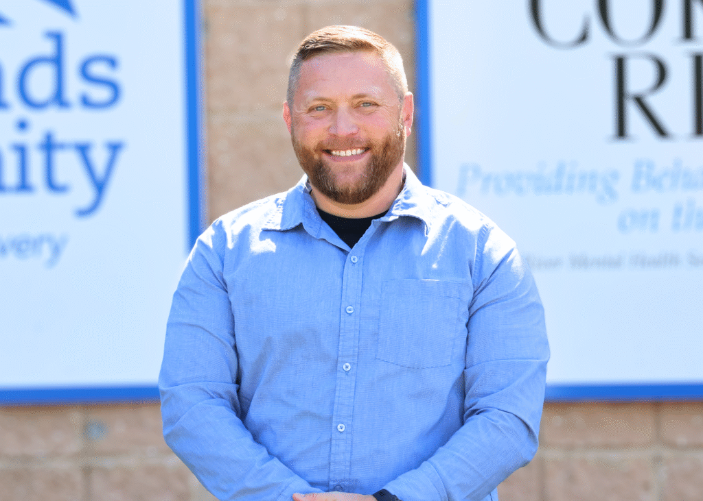 Kyle Willey, Strategy & Communications Director, smiling in front of Crossroads Community and Corsica River signage.